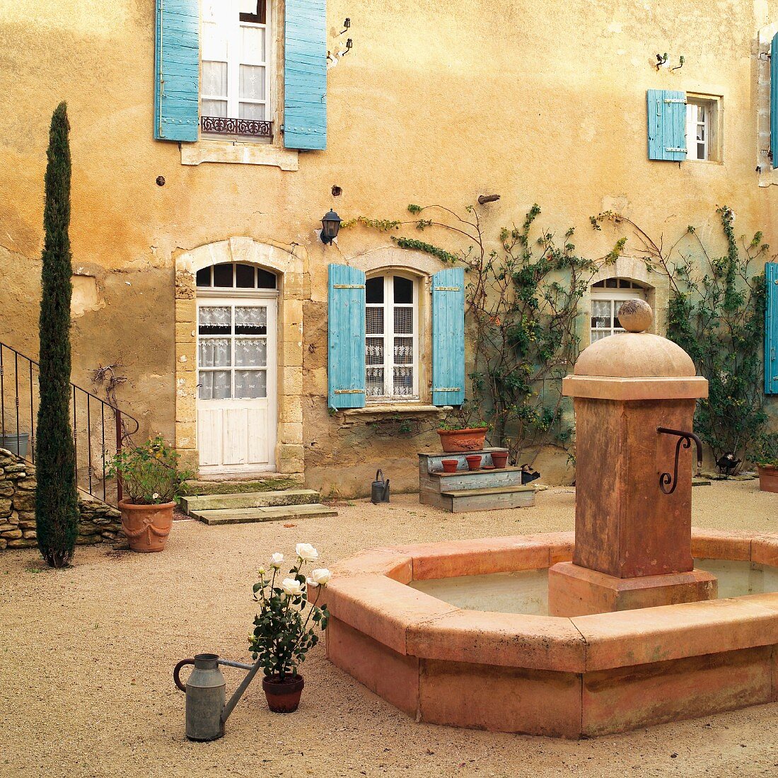 Brunnen im Innenhof eines französischen Landhauses mit türkisblauen Fensterläden an verwitterter Fassade