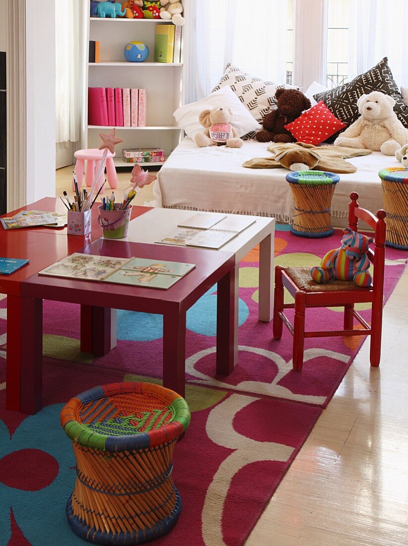 Colourful children's table and chairs; soft toys and cushions on bed in background