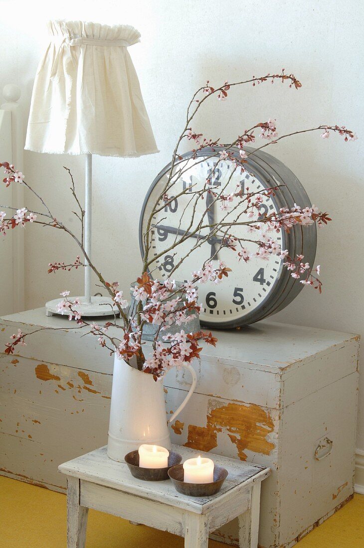 Branches of cherry blossom in vintage jug in front of station clock on old trunk