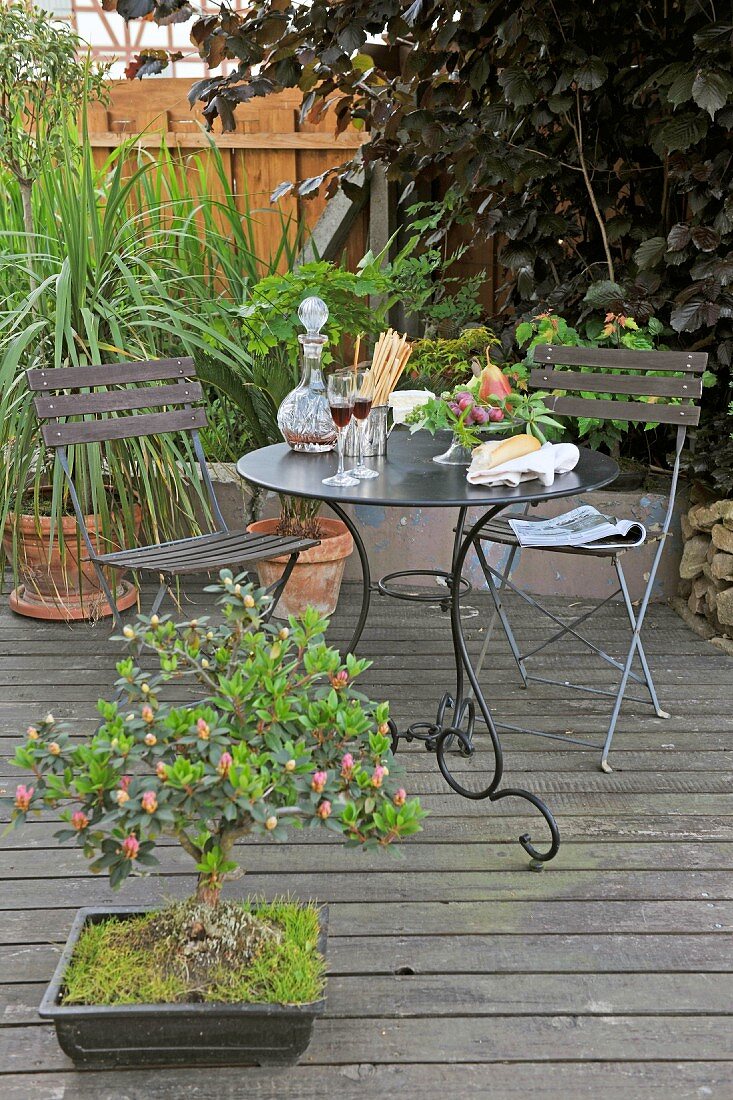 Gartentischset aus dunklem Metall und Bonsaibäumchen auf Holzdeck im Garten