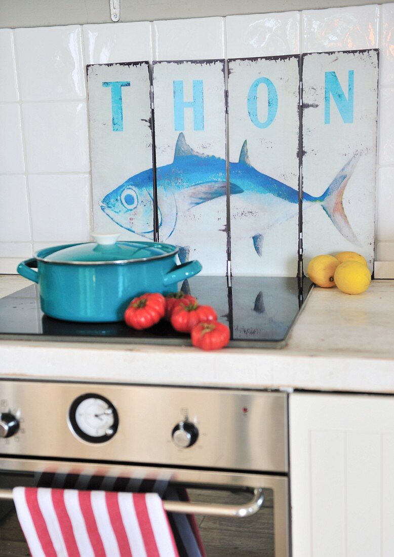 Light blue saucepan on cooker in front of vintage sign with fish motif