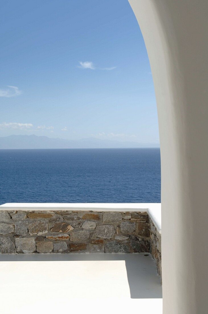 Blick durch Rundbogen über Terrasse mit Natursteinmauer auf das Meer