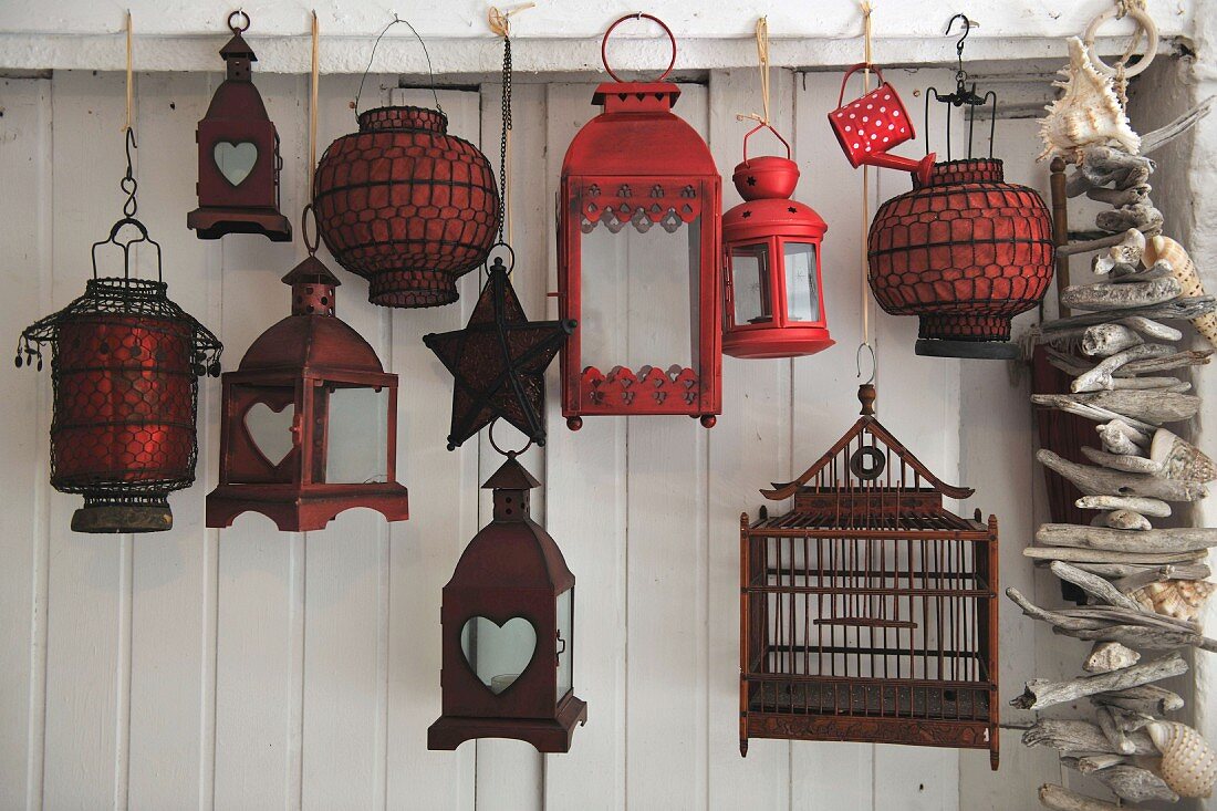 Lanterns of various styles hanging in front of a white wooden wall