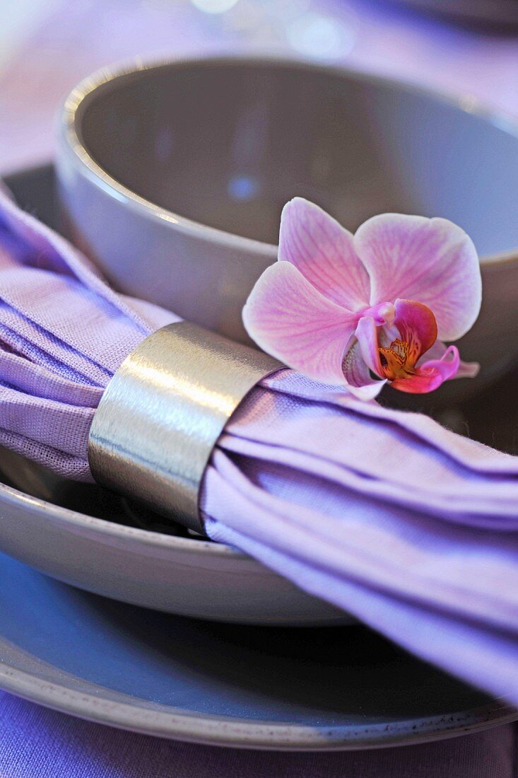 Gedeck mit Serviette und silbernem Serviettenring dekoriert mit violetter Blüte
