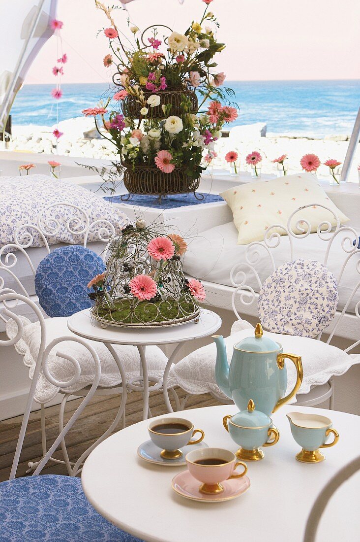 Kaffeetisch mit edlem Kaffeegeschirr; dahinter Blumenarrangements mit pinkfarbenen Gerberablüten
