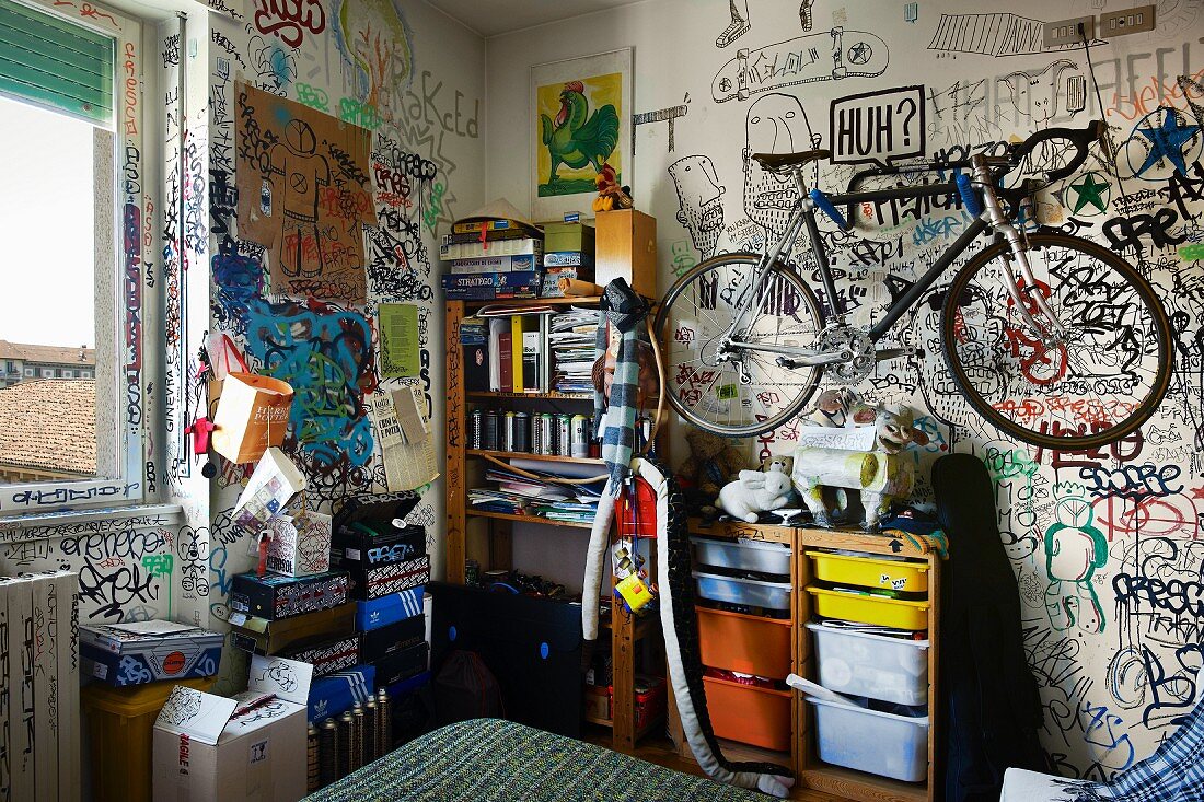 Bike hanging on graffitied wall above shelves in teenager's bedroom
