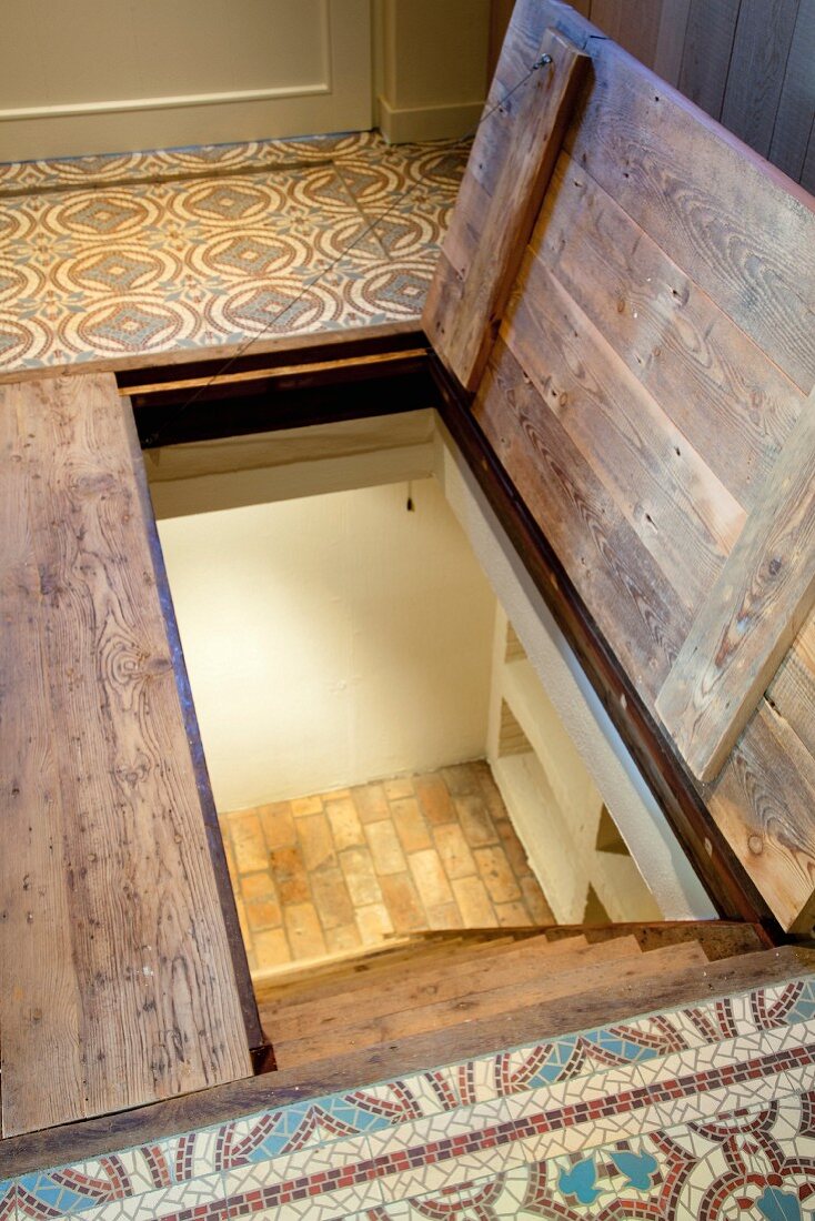 View down steep steps through half-open cellar hatch in floor with patterned tiles