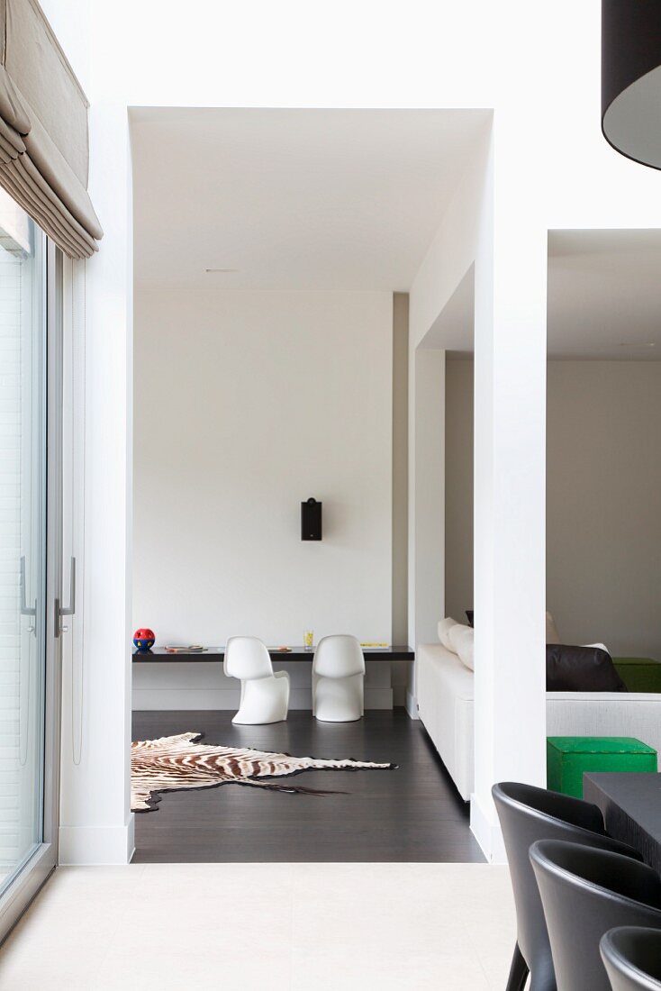 Contemporary interior with perspectives - seating area next to floor-to-ceiling open doorway and view of zebra-skin rug on dark floor in front of white classic shell chairs