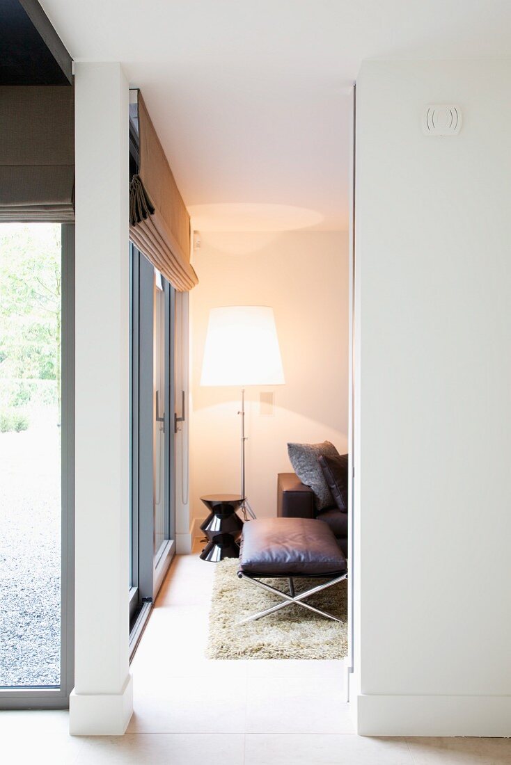 View through floor-to-ceiling doorway of lit standard lamp in corner of contemporary house