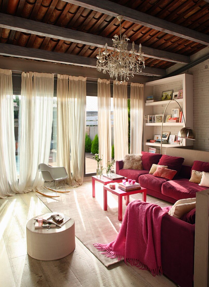 Elegant living room with pink sofa in front of large windows with floor-length curtains