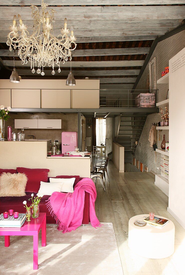 Rosa Polstersofa und pinkfarbener Couchtisch in offenem Wohnraum mit Küchenbereich