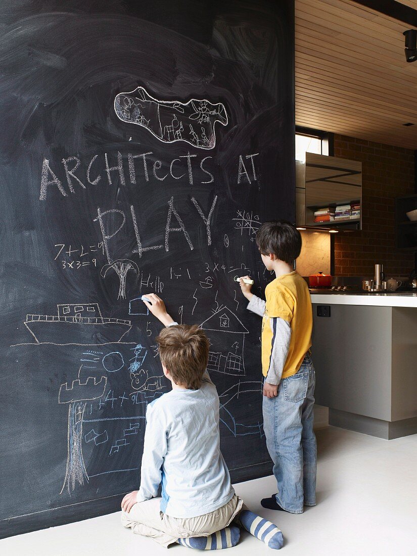 Children drawing on floor-to-ceiling blackboard partition next to kitchen
