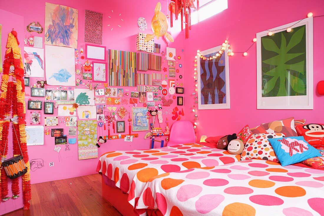 Girl's bedroom with pink walls, twin beds, colourful items decorating walls and fairy lights