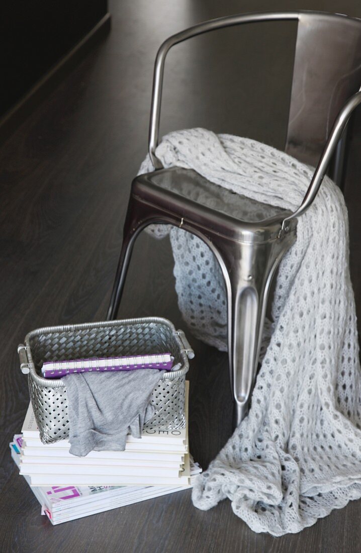 White crochet blanket on metal chair, open basket and books on floor