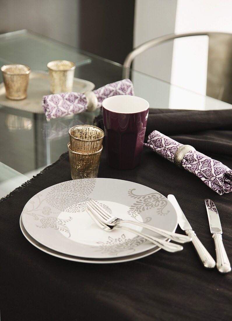 Plate, cutlery, napkin, beaker and tealight holder on table runner