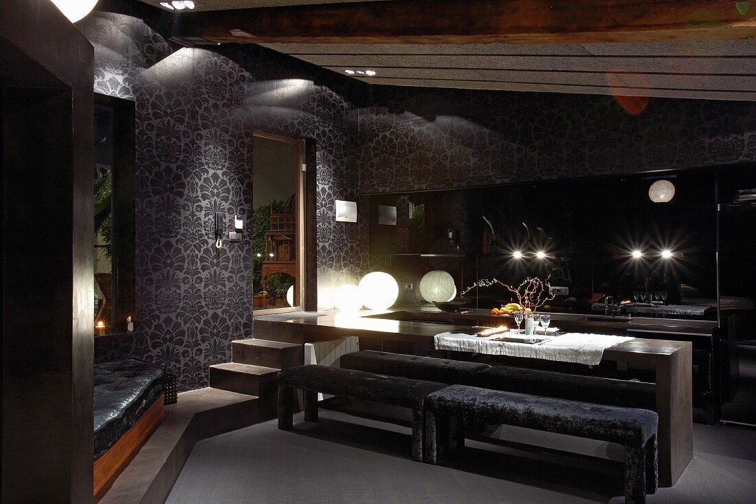 Minimalistischer Esstisch mit gepolsterten Bänken vor offener Küche im Wohnraum mit dunklen Farben