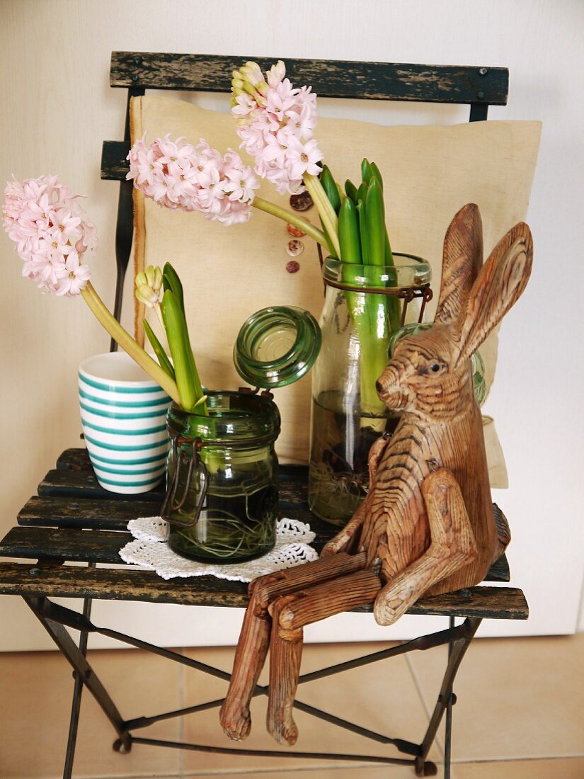 Wooden hare figurine next to glass jars of flowers on rustic folding chair