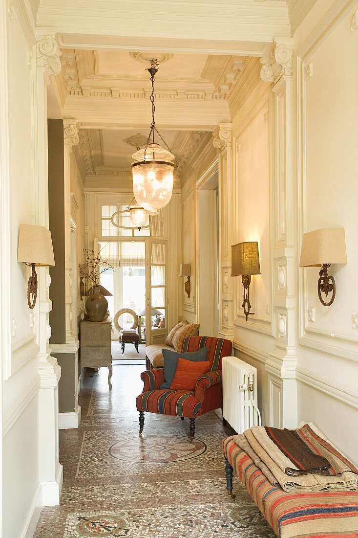 Hallway with stylish sconce lamps and delicate upholstered furnishings on original mosaic floor