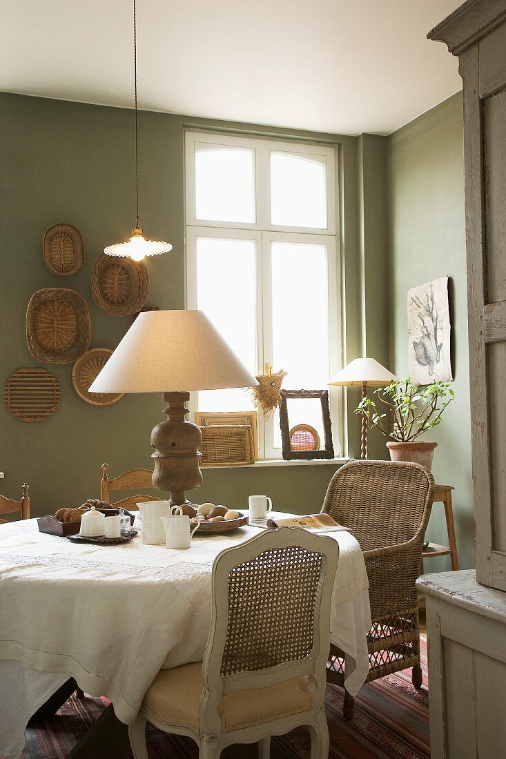 Comfortable dining room with various antique chairs at round table and table lamp with turned wooden base