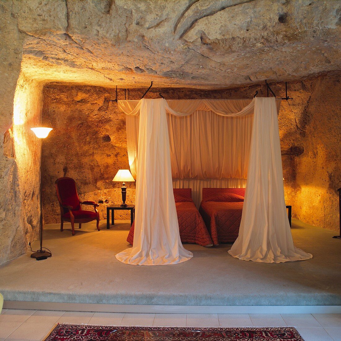 Open-plan sleeping area on platform - twin beds with canopy and lit table lamps in grotto-style niche
