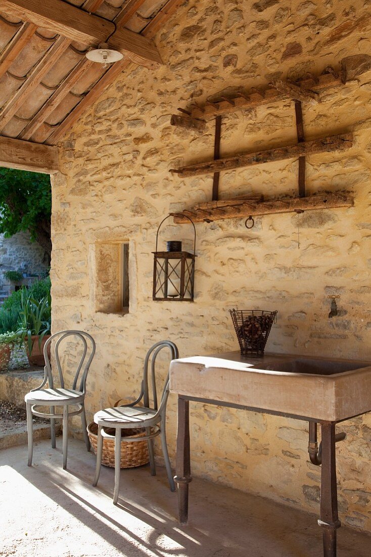 Trough sink next to grey-painted Thonet chairs in front of stone outer wall of Mediterranean house