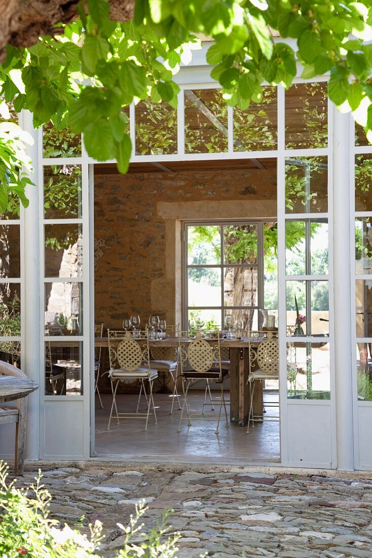 Blick durch offene Glasterrassentür eines mediterranen Landhauses auf gedecktem Esstisch
