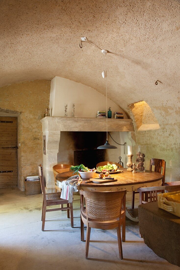 Round table in front of open fireplace and below pendant lamp in simple dining room with barrel vault ceiling