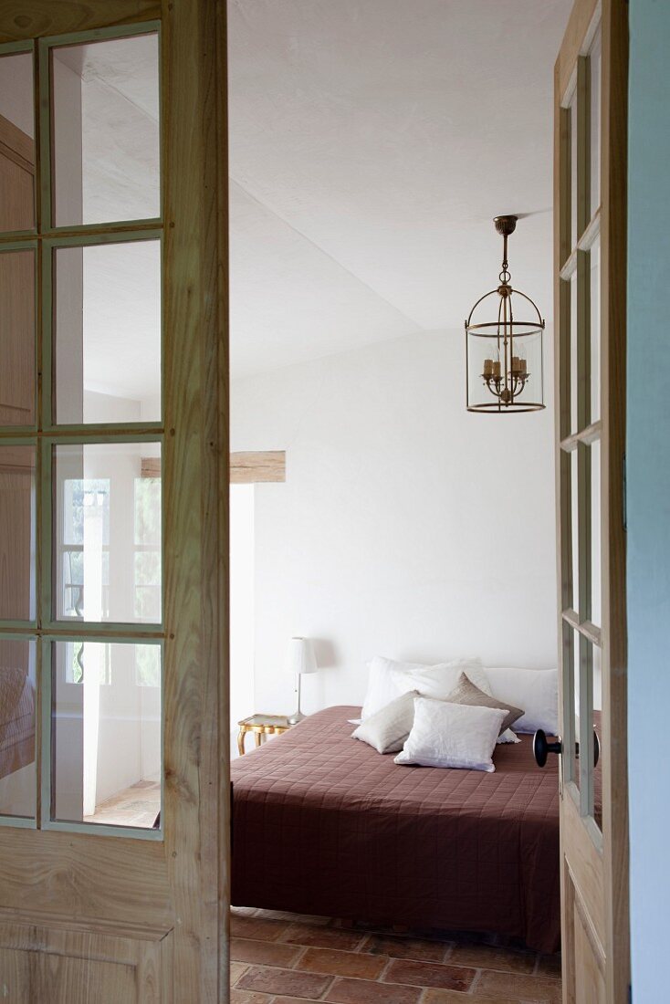 View through open lattice door of modern double bed with scatter cushions in simple bedroom