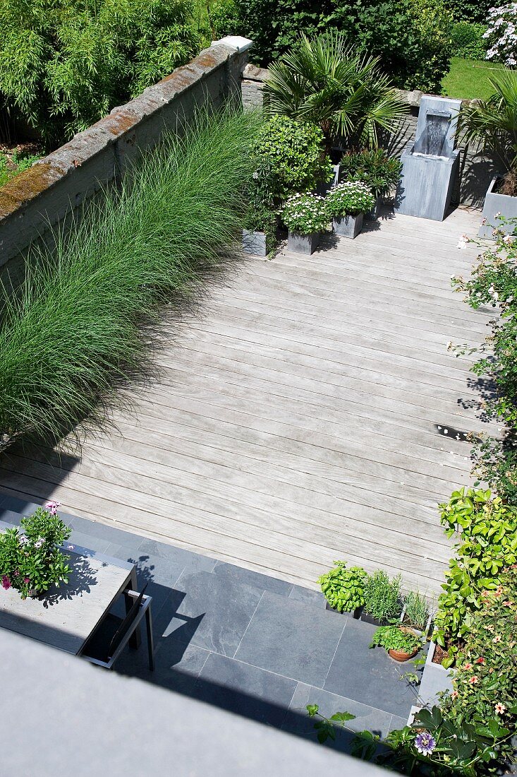 View down onto modern wooden terrace with ornamental grasses and planters against stone wall