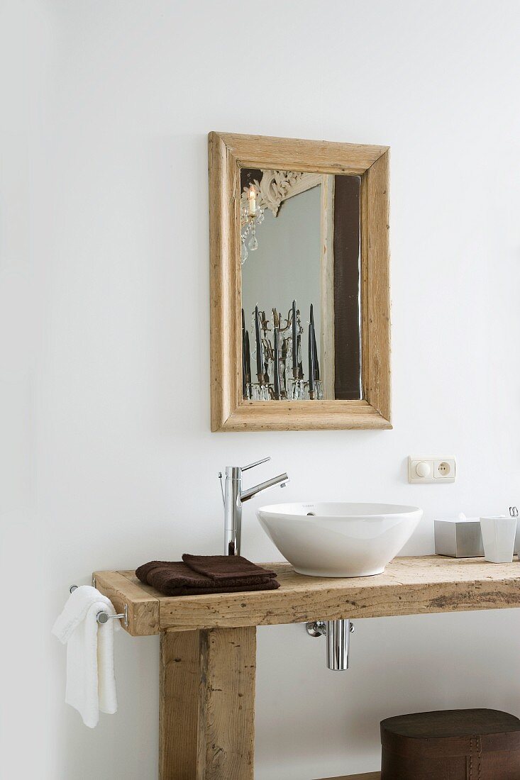 Rustikaler Waschtisch mit Waschschüssel auf Holzplatte und Designer Armatur vor Wand mit gerahmtem Spiegel