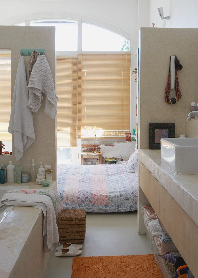 Blick aus offenem Waschbereich - Bett auf Boden vor geschlossener Bambusjalousie am Fenster in loftähnlichem Wohnraum
