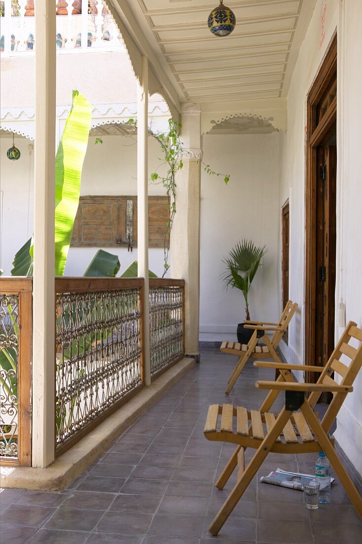 Offener umlaufender Laubengang mit schlichten Holzstühlen an Wand und Blick in Innenhof