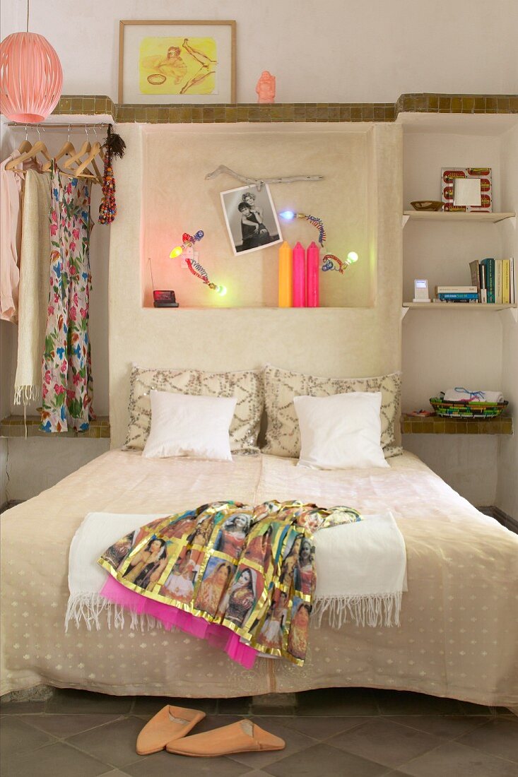 Orientalisches Kleid auf Doppelbett an Wand mit beleuchteter Wandnische in schlichtem Schlafzimmer