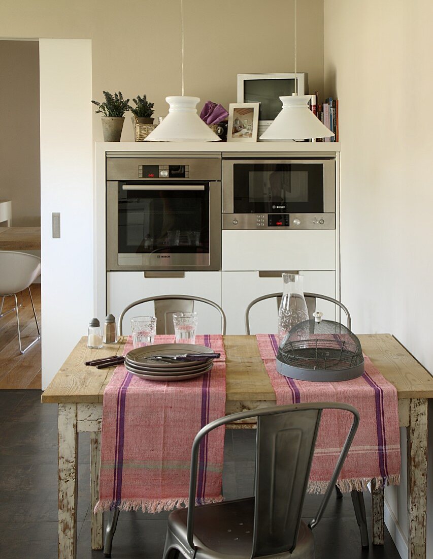 Rustikaler Küchentisch mit Tischläufern und Geschirr vor modernem Schrank mit Einbaugeräten