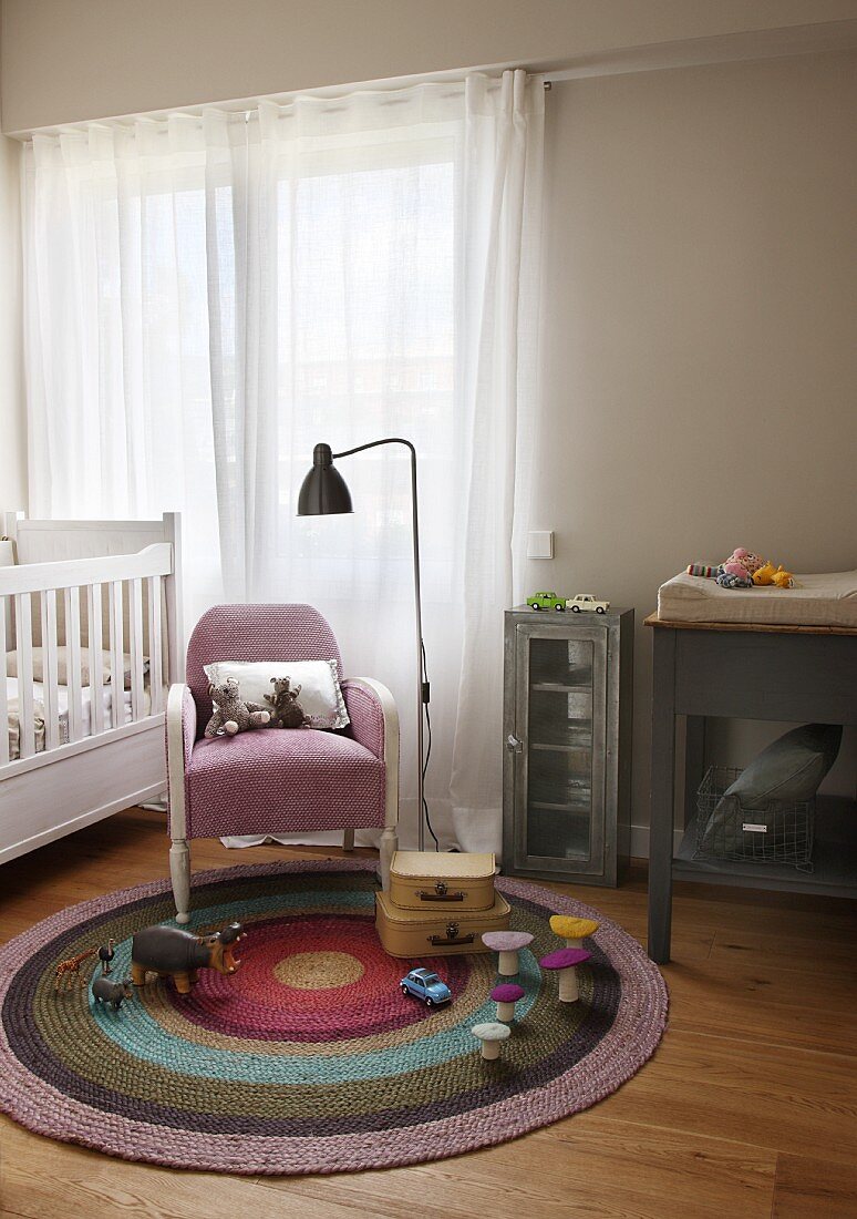 Retro Stehlampe neben Sessel und Spielsachen auf rundem Teppich in schlichtem Kinderzimmer