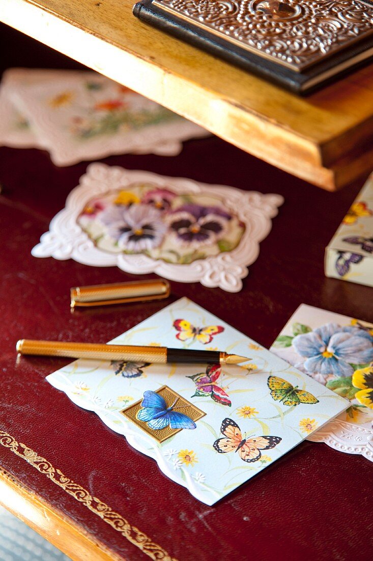 Various greetings cards with butterfly motifs and gold fountain pen on claret red leather desk blotter