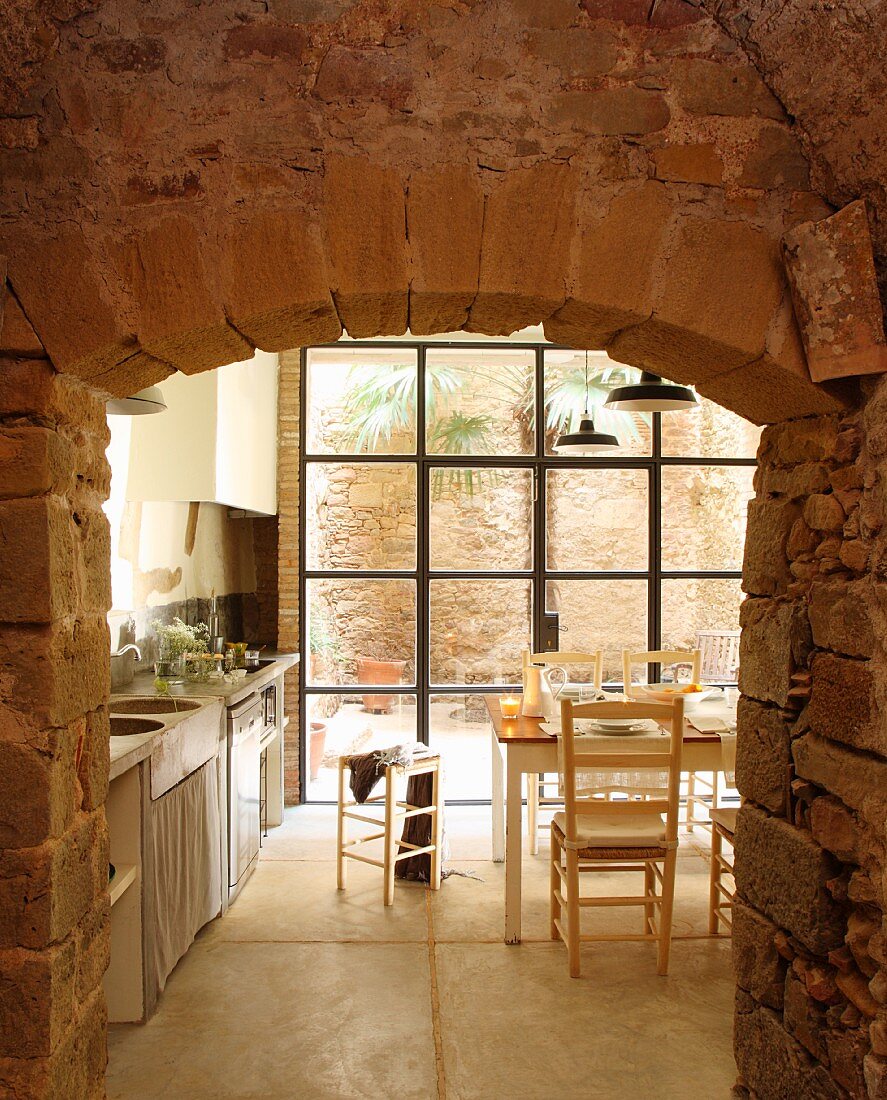 Blick durch Naturstein Durchbruch ins Esszimmer mit Küche auf Tisch vor Terrassentür