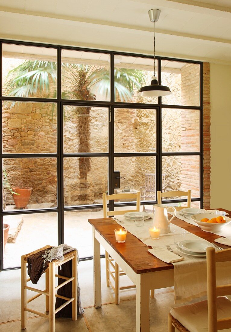 Gedeckter Esstisch mit Teelichtern vor Terrassentür und Blick in Innenhof auf Palme