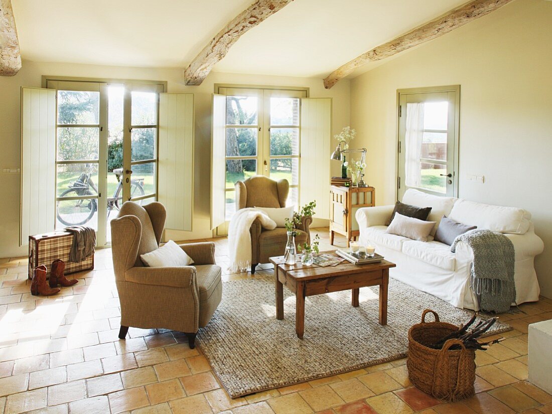 Simple interior with view of garden - wooden table between wingback chairs and couch in Mediterranean country house