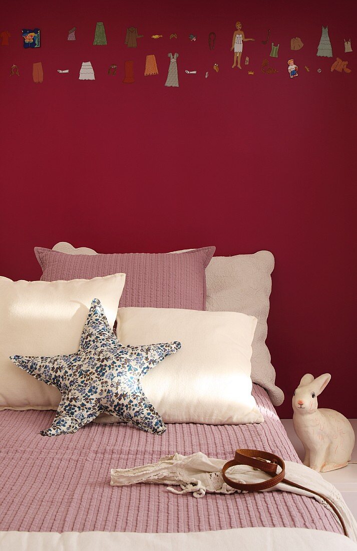 Bed decorated in cream and dusky pink with starfish cushion and rabbit ornament against wall painted dark red with row of painted miniature figures