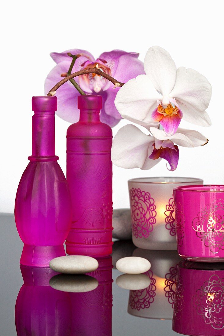 Pinkfarbene Flaschen mit Orchideenzweig dekoriert und Windlichter