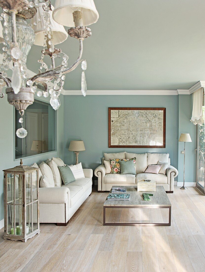 Deckenkerzenleuchter und Loungeecke mit weisser Polstergarnitur vor hellblau getönten Wänden und modernem Couchtisch in traditionellem Ambiente
