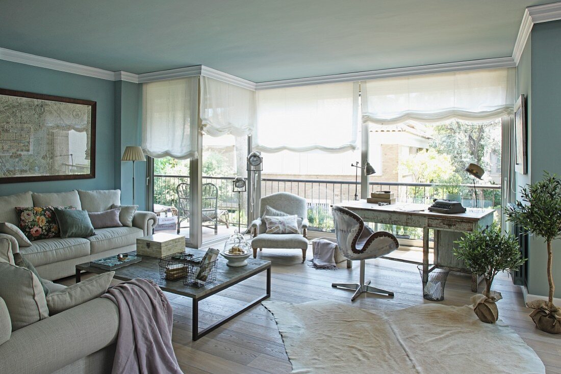 Grosszügiges Wohnzimmer mit Loungeecke und Arbeitstisch vor Fensterfront und halboffenem Raffrollo