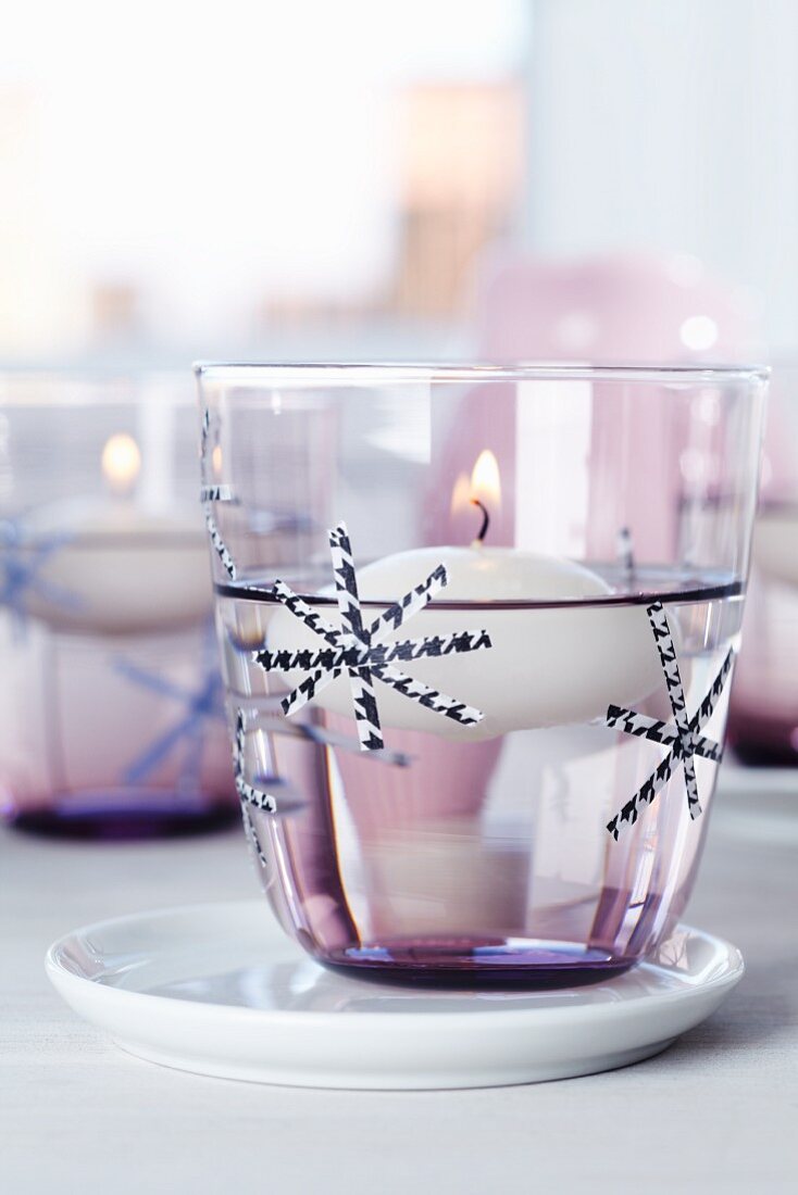 Stylised snowflakes made from thin strips of tape decorating candle lantern with floating candle