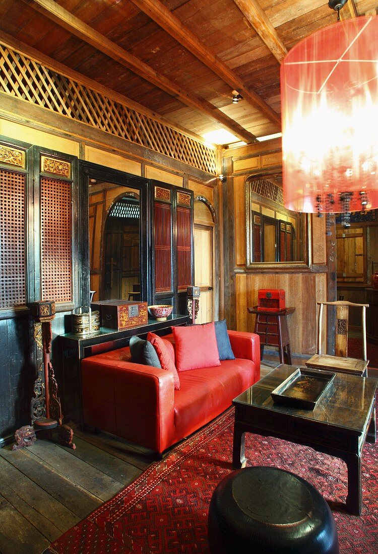 Asiatische Lounge mit Holzgitterwänden und roter Ledercouch vor schwarzem Couchtisch auf Teppich