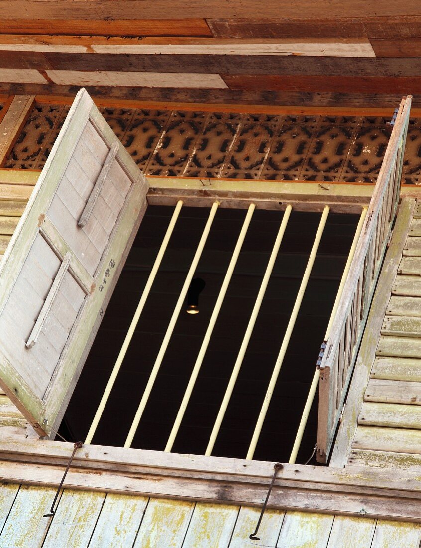 Offene Fensterläden an vergittertem Fenster eines traditionellen, asiatischen Holzhauses