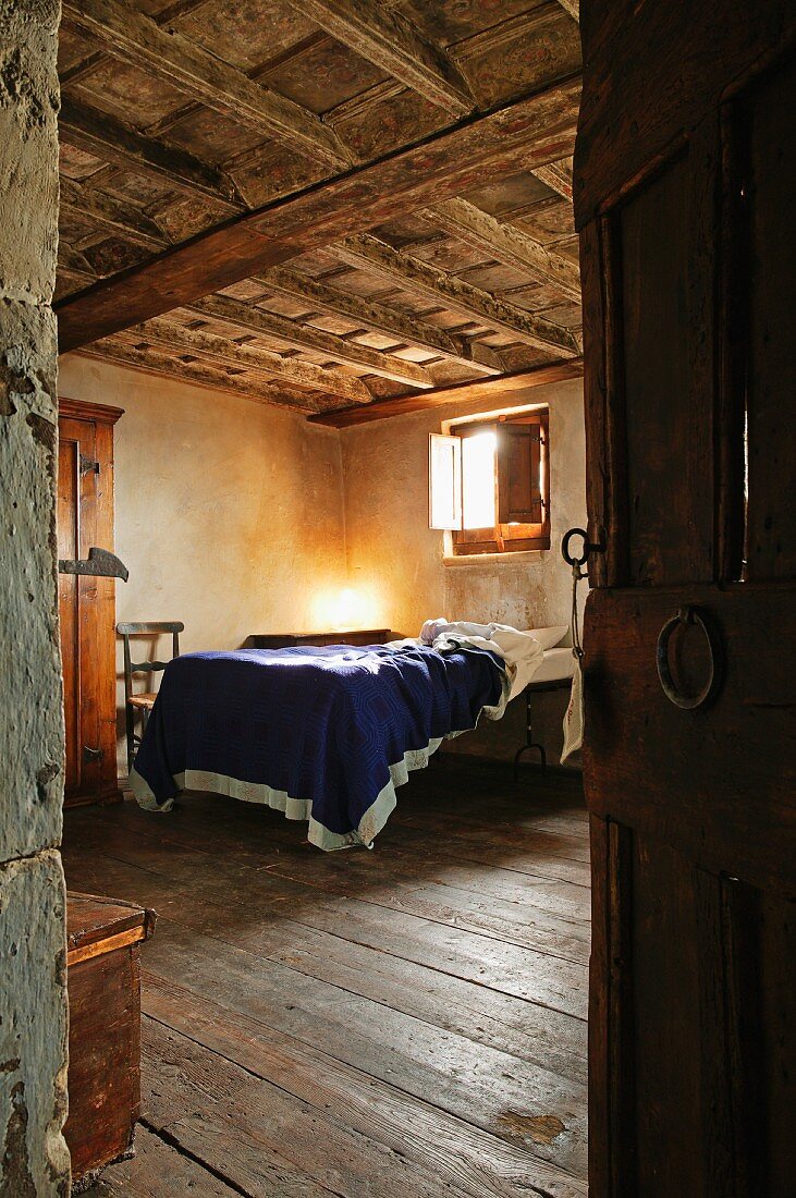 View of bed in rustic bedroom with wooden coffered ceiling through open door