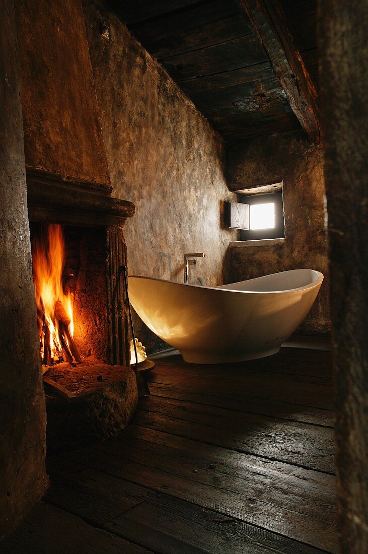 Atmospheric old room with open fire next to free-standing designer bathtub