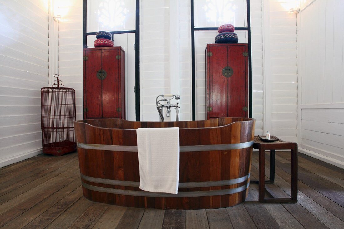 Freistehende Holzzuber-Badewanne vor Schränken in asiatischem Stil an weisser Holzwand