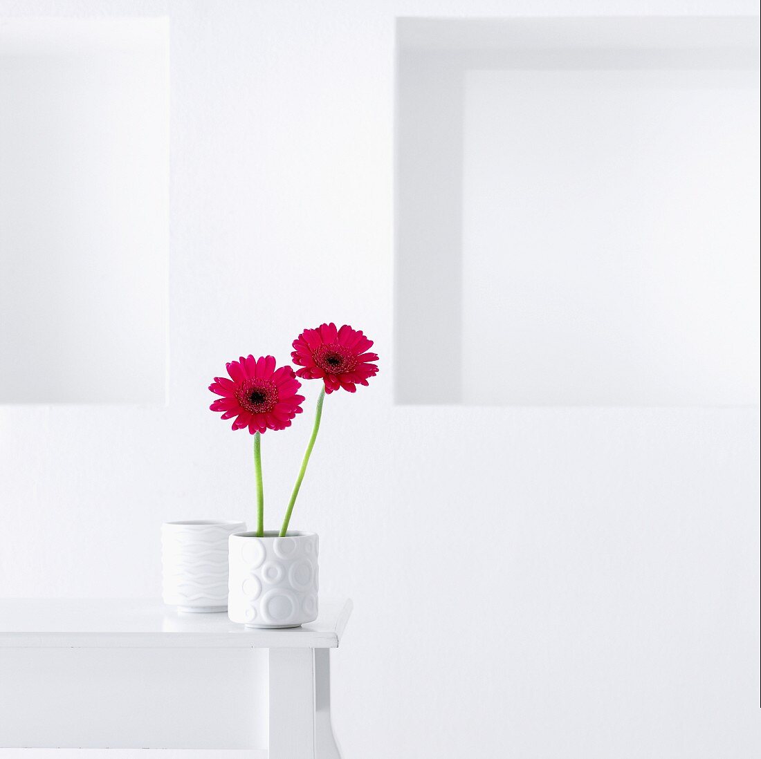 Pinkfarbene Gerbera in weisser Vase auf Tisch vor weisser Wand